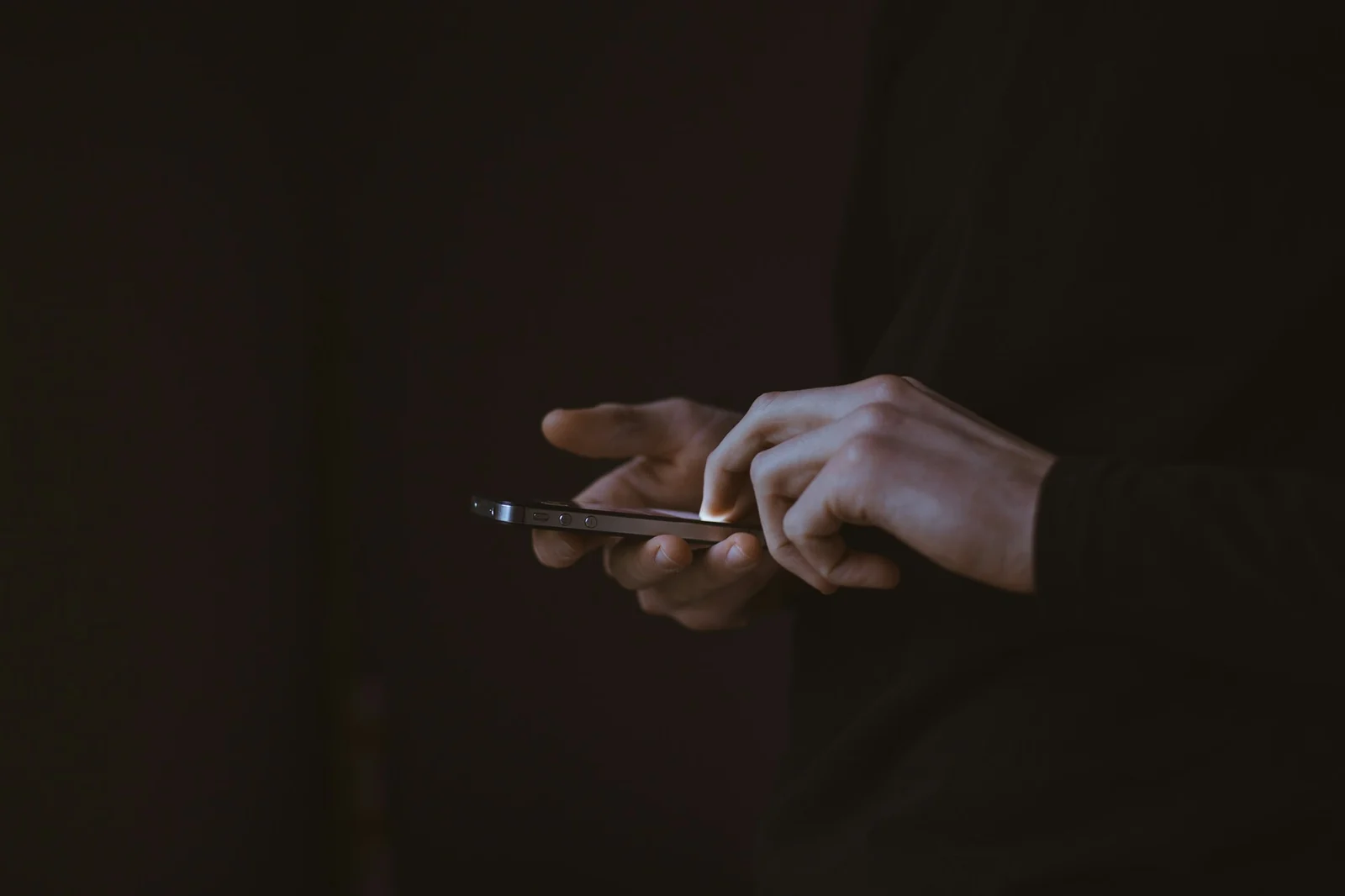 Hands holding a smartphone in a dark room, the personal phone at the centre of most domestic violence digital forensics