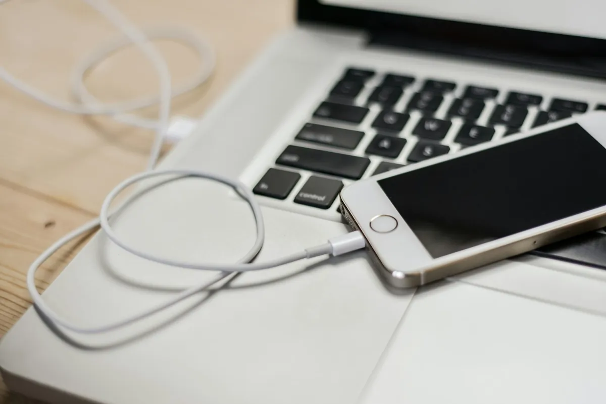 iPhone resting on a MacBook with a white cable plugged in, a reminder that a computer backup can survive a factory reset